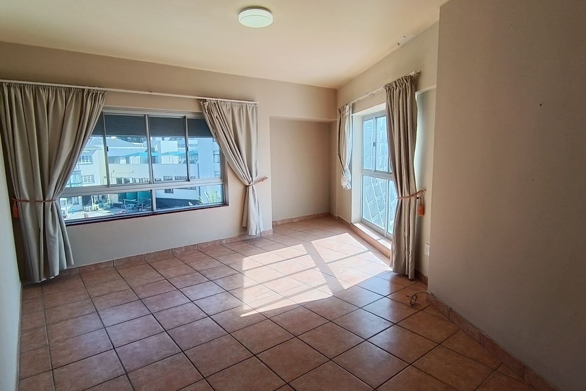 A bright, empty living room featuring tiled flooring and large windows with natural light, offering a blank canvas for interior design.