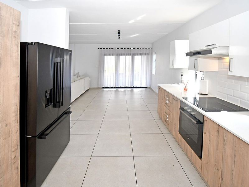 Modern open-plan kitchen and living area featuring sleek cabinetry, integrated appliances, tiled flooring, and direct access to the outdoor space through sliding doors.