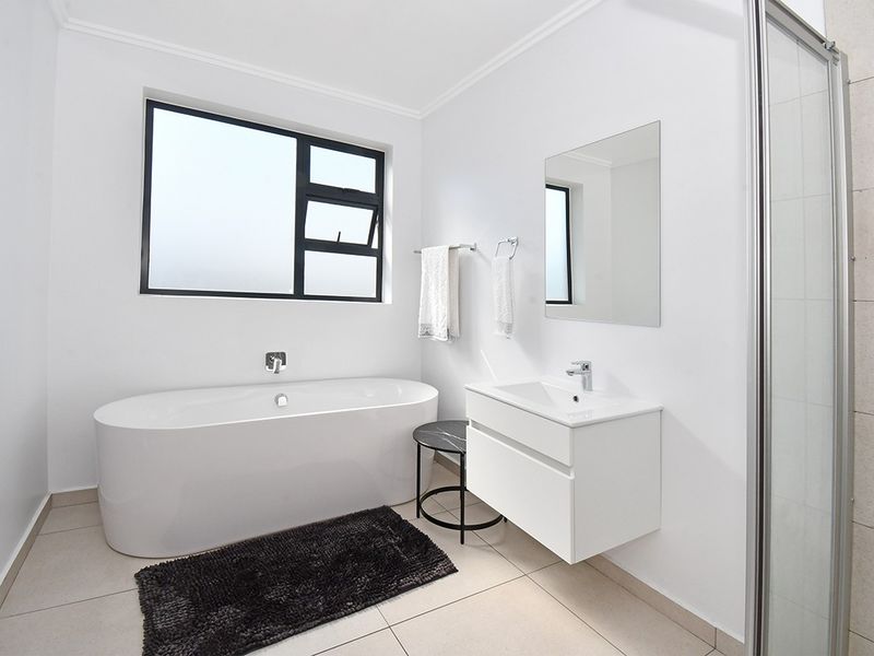Modern bathroom featuring a sleek freestanding bathtub, wall-mounted vanity with basin, and a separate shower enclosure with neutral floor tiling.