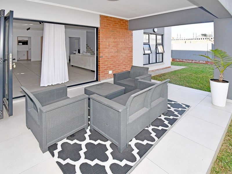 A covered patio area featuring tiled flooring and an exposed brick wall, seamlessly connecting to the interior living space through large bi-fold doors.