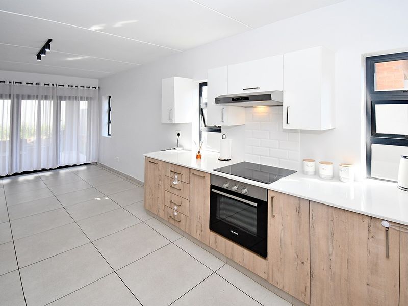 Modern open-plan kitchen and living area featuring light wood-finish cabinetry, white countertops, subway tile backsplash, and large sliding doors leading to the exterior.