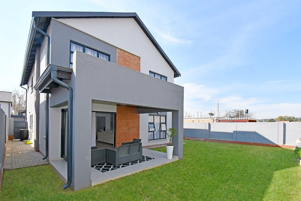 Rear view of a modern double-story house featuring a covered patio, brick and plaster exterior finishes, and a well-maintained lawn.