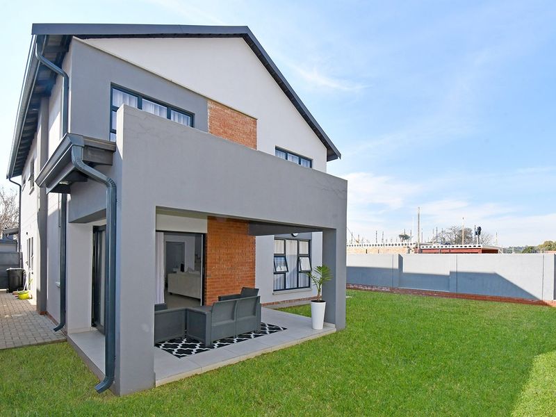 Rear view of a modern double-story house featuring a covered patio, brick and plaster exterior finishes, and a well-maintained lawn.