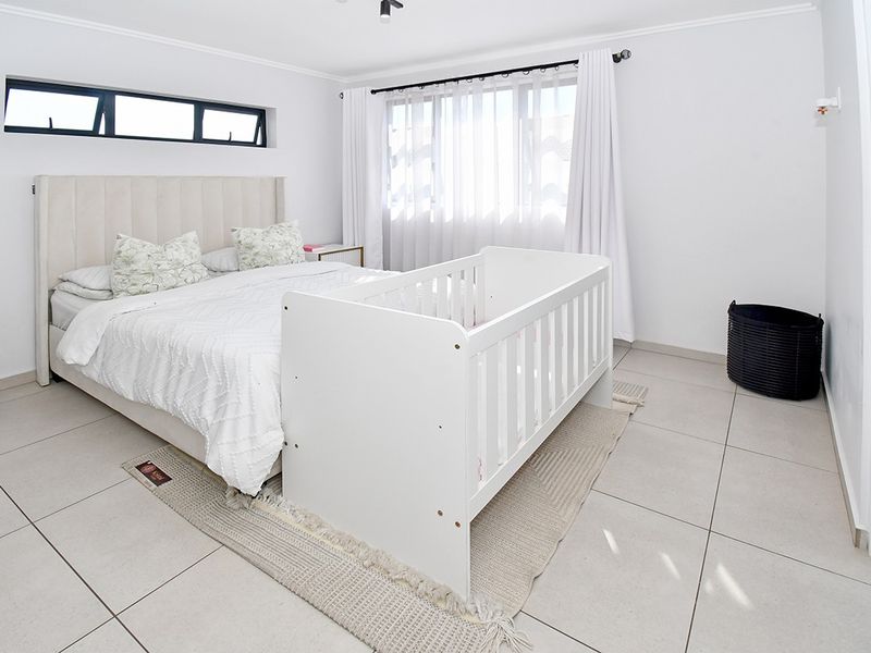 A bright and spacious bedroom featuring neutral tiled flooring, a large window with curtains, and an additional clerestory window for extra natural light.