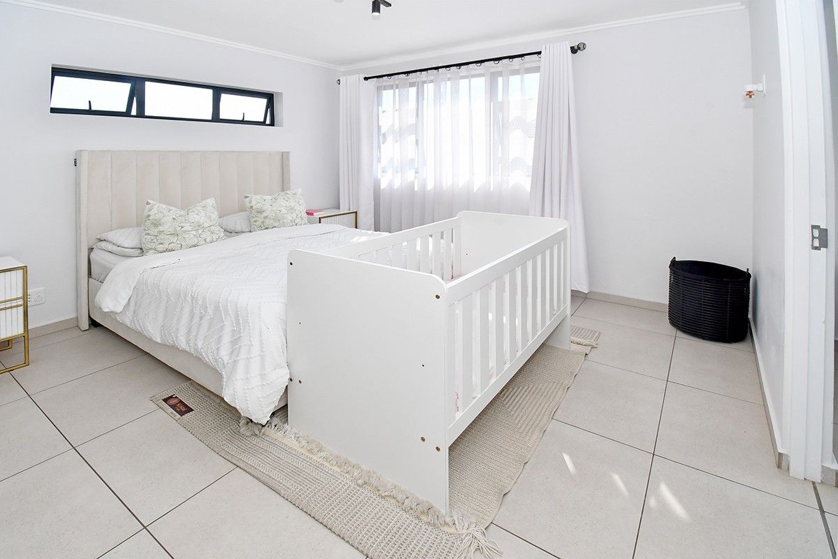 A bright and spacious bedroom featuring neutral tiled flooring, a large window with curtains, and an additional clerestory window for extra natural light.