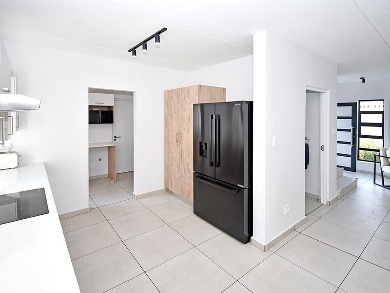 Modern kitchen featuring clean white cabinetry, integrated hob, extractor fan, and neutral tiled flooring, leading into a scullery and adjacent living area.