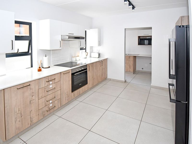 Modern kitchen featuring light wood-grain cabinetry, white stone countertops, subway tile backsplash, and integrated appliances, with an adjacent scullery area.
