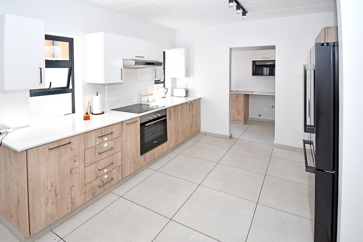 Modern kitchen featuring light wood-grain cabinetry, white stone countertops, subway tile backsplash, and integrated appliances, with an adjacent scullery area.
