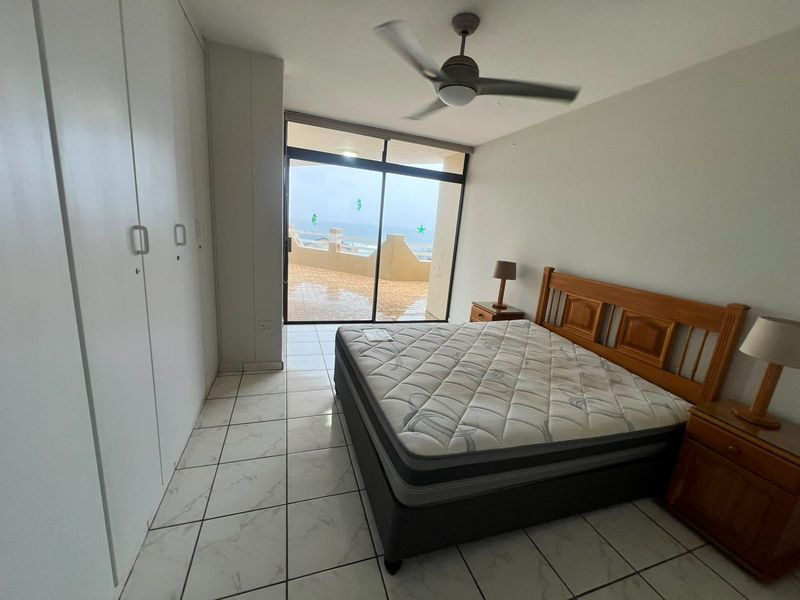 Bedroom featuring tiled flooring, built-in cupboards, a ceiling fan, and a sliding glass door providing access to a balcony with ocean views.