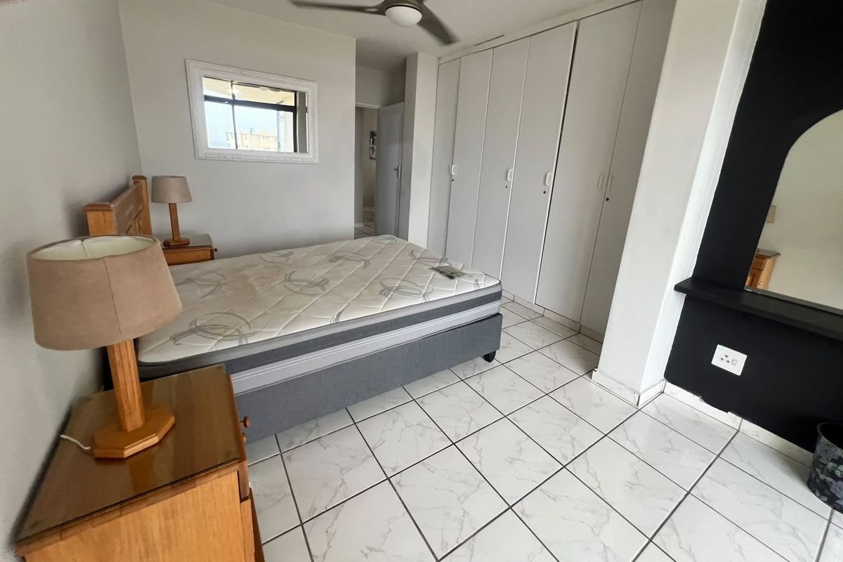 A bedroom featuring white tiled flooring, built-in cupboards, and a ceiling fan, offering a functional space with neutral finishes.