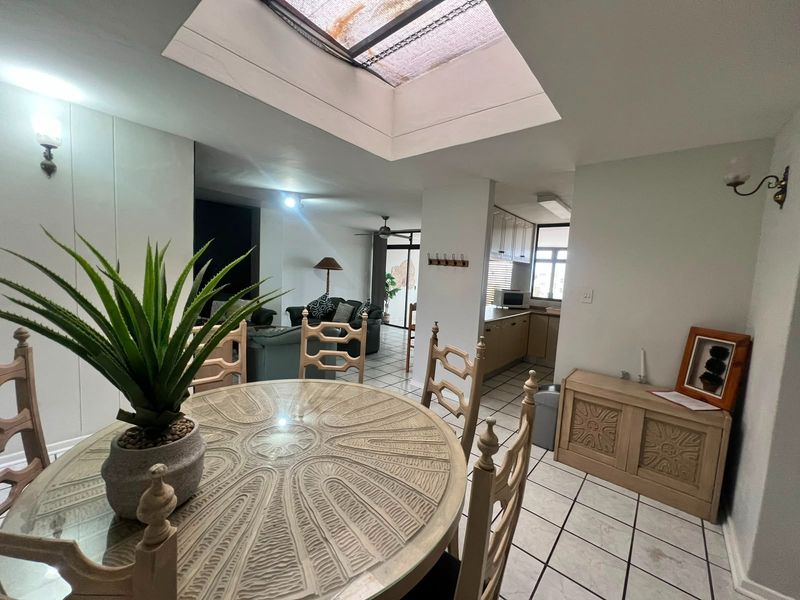Open-plan living and dining area featuring tiled flooring, a central skylight, and an adjacent kitchen with built-in cabinetry.