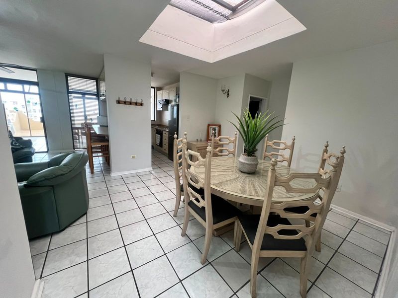 Open plan living and dining area featuring ceramic tile flooring, a central skylight, and direct access to an adjoining kitchen and outdoor balcony.