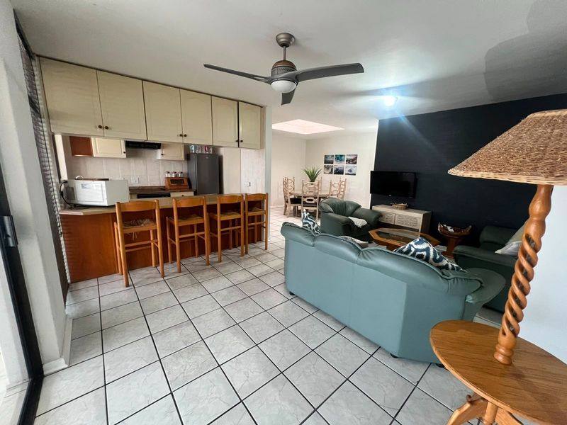 Open-plan living and kitchen area featuring tiled flooring, a breakfast bar, built-in cabinetry, and a ceiling fan, with a dining space beyond.