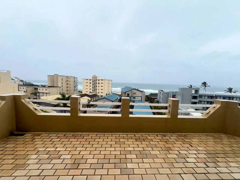 An open balcony featuring brick paving and a masonry balustrade, offering expansive coastal and neighbourhood views.