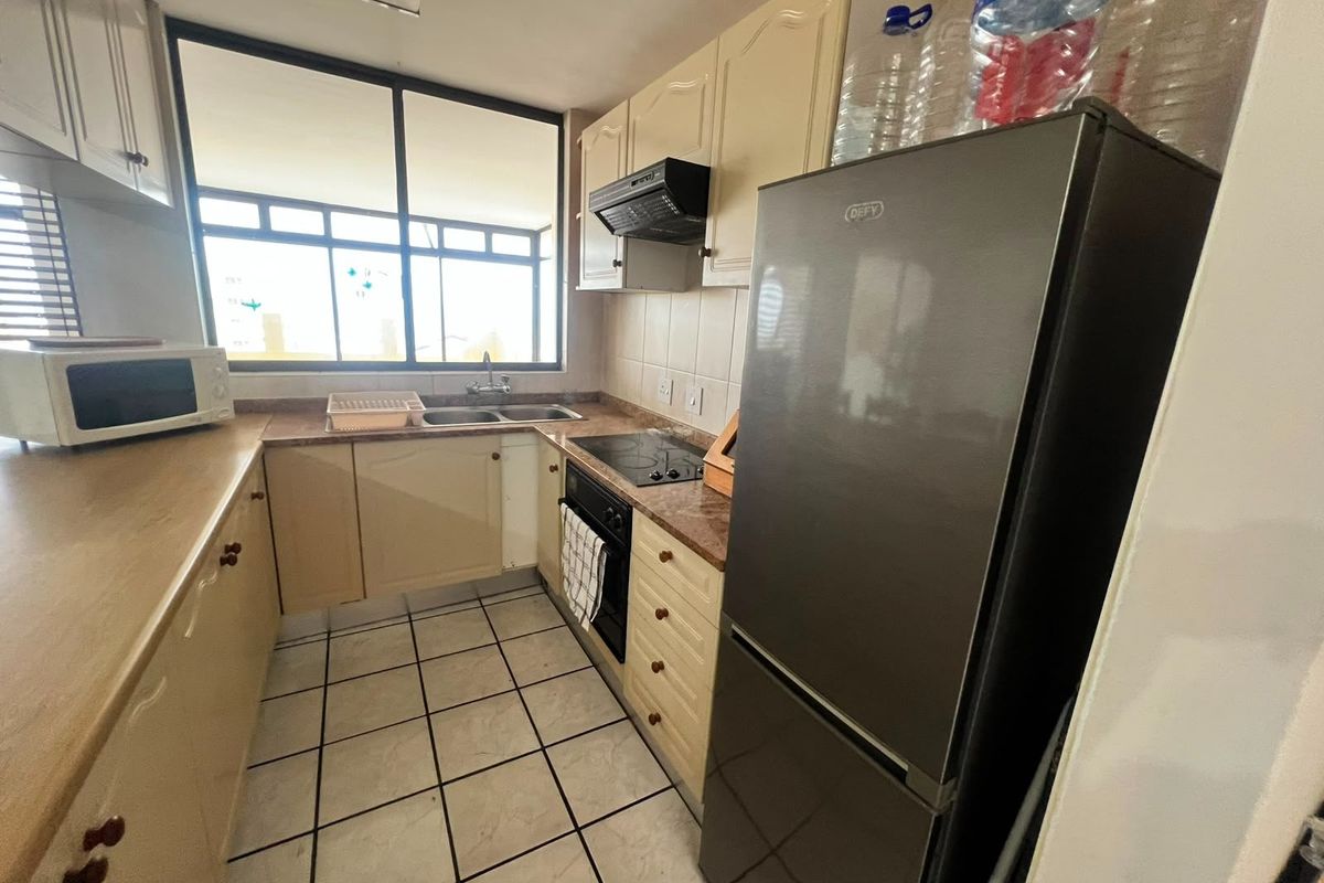 Compact kitchen featuring built-in cabinetry, laminate countertops, a double basin sink, and integrated cooking appliances with tiled flooring and backsplash.