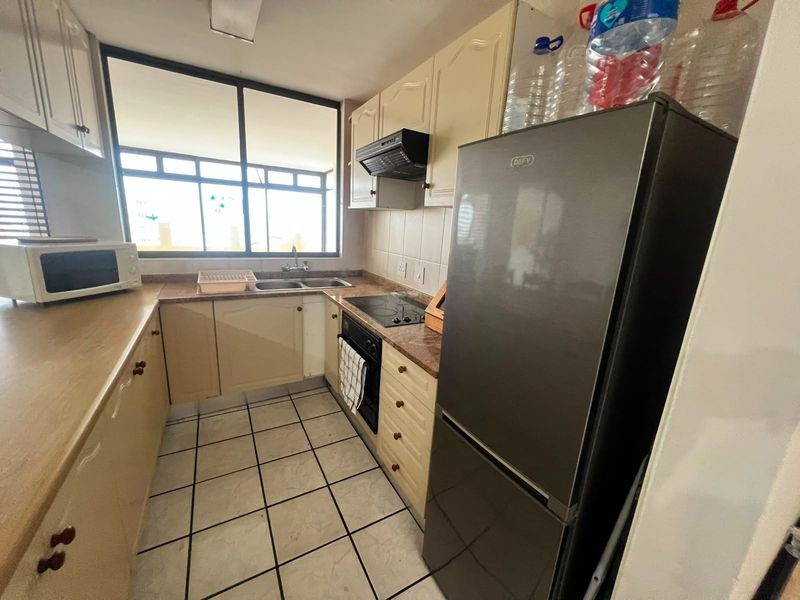 Compact kitchen featuring built-in cabinetry, laminate countertops, a double basin sink, and integrated cooking appliances with tiled flooring and backsplash.