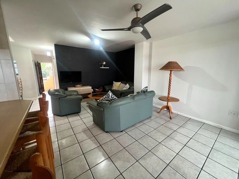Open-plan living area featuring tiled flooring, a ceiling fan, and a dark accent wall, with an adjacent breakfast bar area.