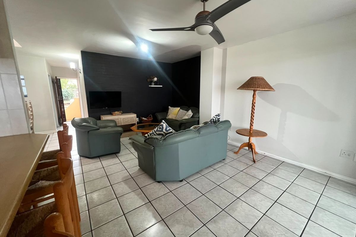 Open-plan living area featuring tiled flooring, a ceiling fan, and a dark accent wall, with an adjacent breakfast bar area.