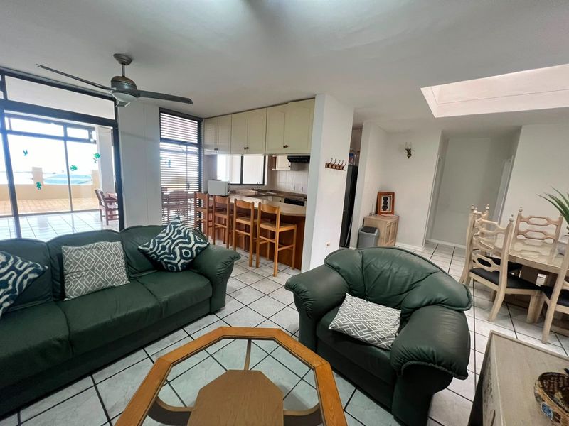Open-plan living and kitchen area featuring tiled flooring, a breakfast bar, ceiling fan, and natural light from a skylight and sliding glass doors.