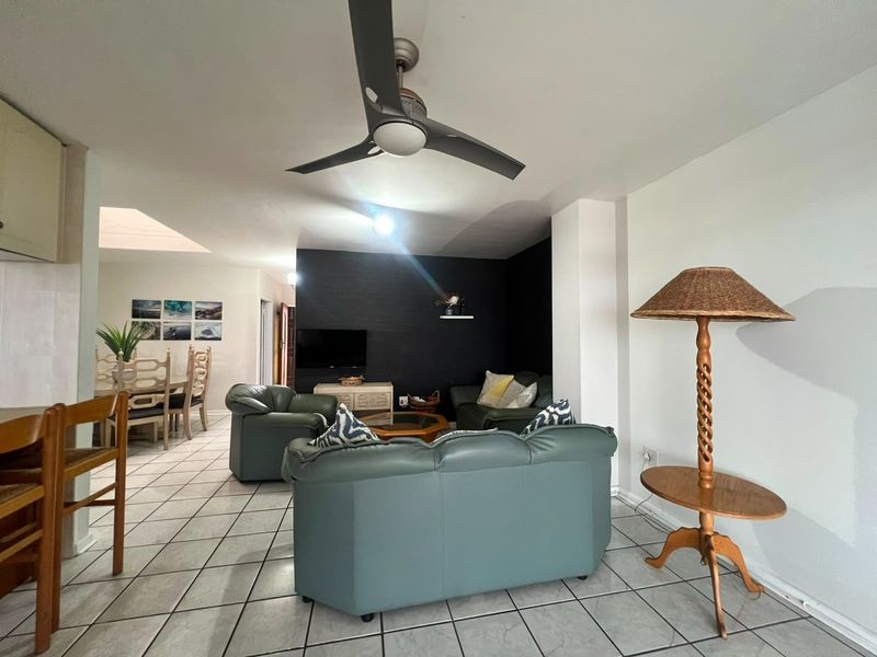 Spacious open-plan living and dining area featuring tiled flooring, a modern ceiling fan, and a dark feature wall.