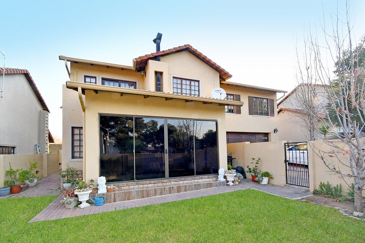 Rear view of a two-story house featuring a tiled roof, large sliding glass doors, and a paved patio area leading to a garden.