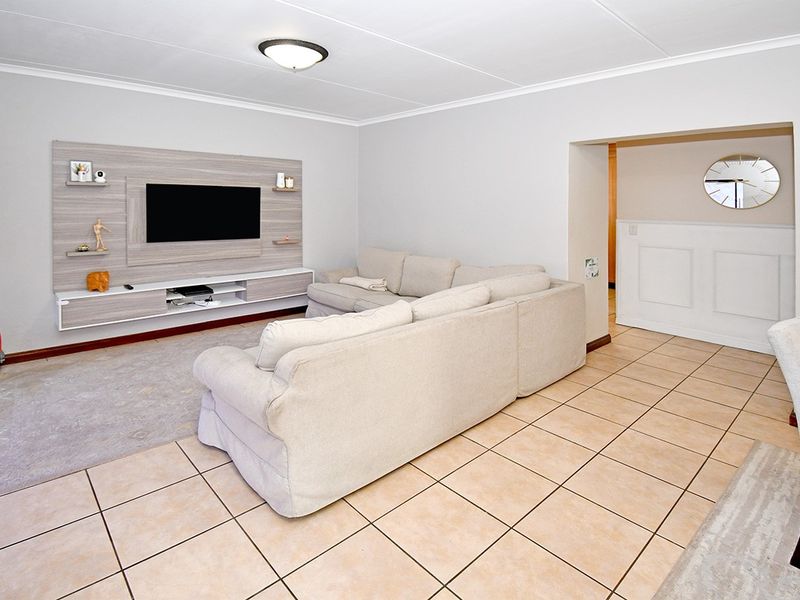 A spacious living room featuring tiled flooring, a modern built-in media unit, and wainscoting detail, offering a comfortable and functional living space.