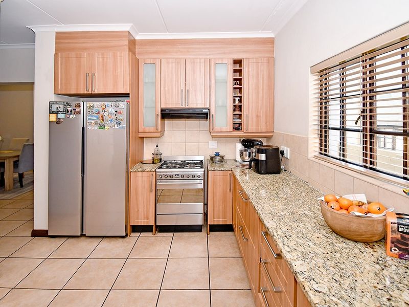 A functional kitchen featuring granite countertops, wood veneer cabinetry, a gas stove with extractor fan, and tiled flooring.