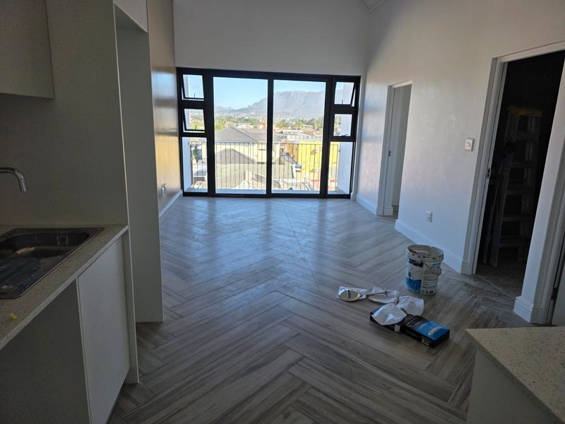 Bright open-plan living area featuring modern herringbone tile flooring, vaulted ceilings, and large sliding doors leading to a balcony with mountain views.