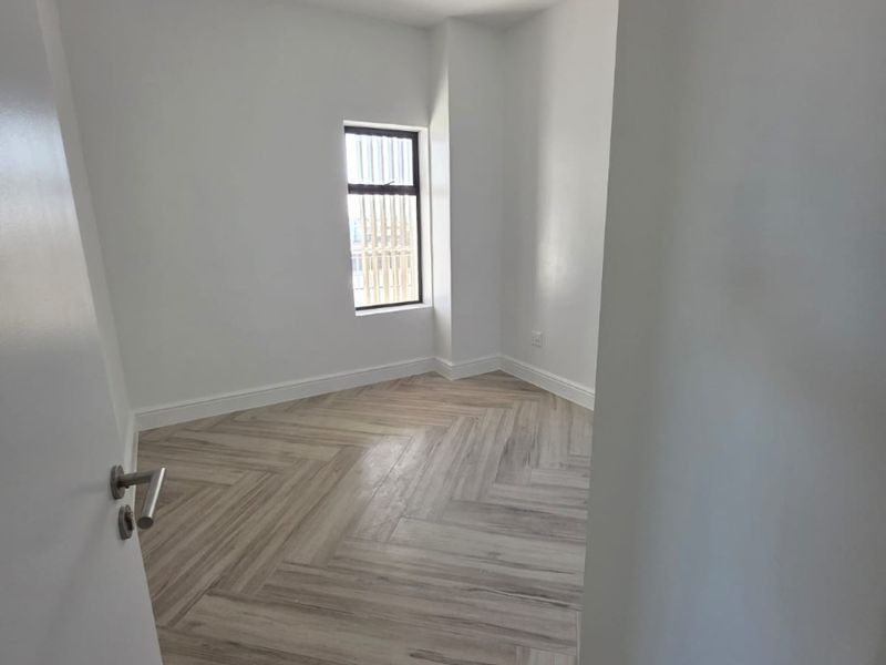 A bright, empty bedroom featuring modern herringbone wood-look tile flooring and a window with security bars.