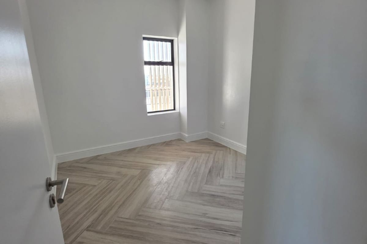 A bright, empty bedroom featuring modern herringbone wood-look tile flooring and a window with security bars.