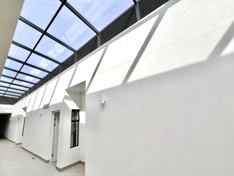 A bright, modern hallway featuring a large glass skylight, tiled flooring, and clean white walls with integrated lighting.