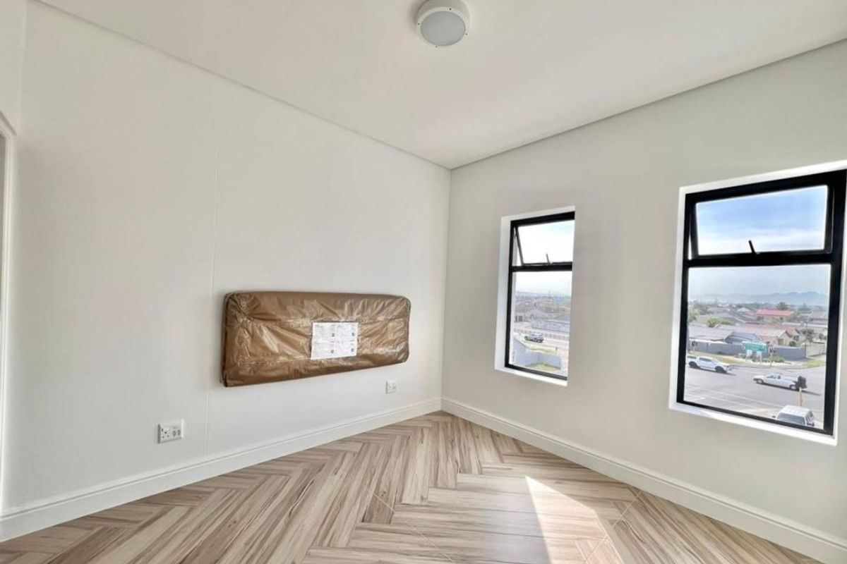 A bright, modern bedroom featuring contemporary herringbone tile flooring, clean white walls, and large black-framed windows offering natural light and neighborhood views.