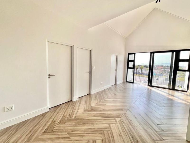 Bright and spacious living area featuring high vaulted ceilings, modern herringbone tile flooring, and large sliding doors leading to a private balcony.