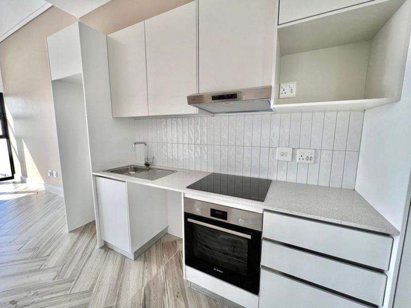 Modern kitchen featuring white cabinetry, stone countertops, integrated electric hob, oven, extractor fan, and stylish herringbone flooring in a clean, contemporary space.