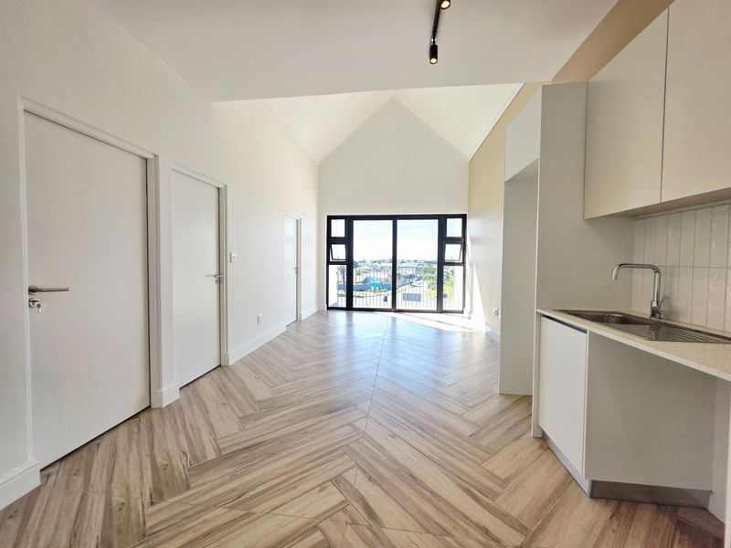 Modern open-plan living area featuring herringbone tile flooring, a sleek kitchen kitchenette, vaulted ceilings, and large sliding doors leading to a balcony.