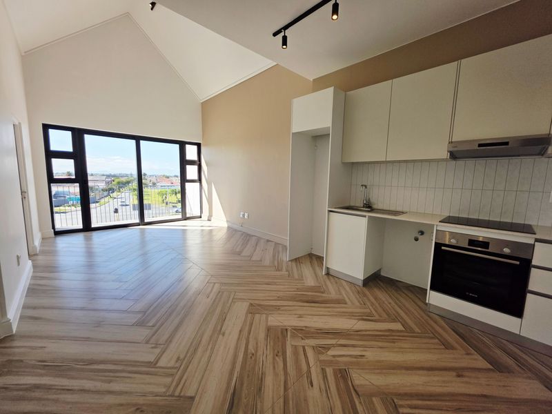 Modern open-plan living area featuring high vaulted ceilings, herringbone tile flooring, and a sleek kitchen with built-in appliances and large sliding doors.