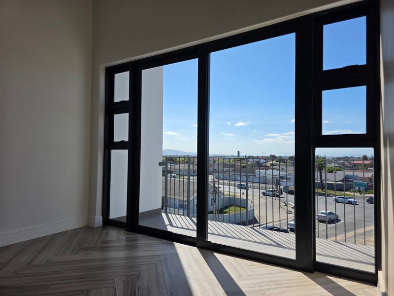 Bright living area featuring modern herringbone flooring and large sliding glass doors opening onto a balcony with expansive neighborhood views.