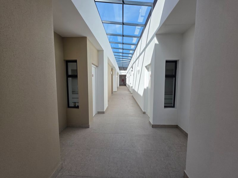 A bright, modern apartment hallway featuring tiled flooring and a full-length glass skylight providing ample natural light.