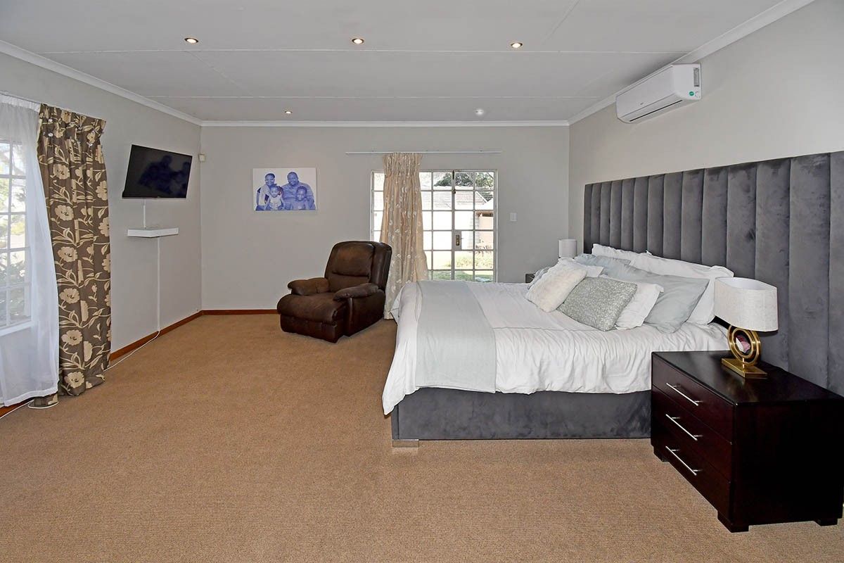 Spacious bedroom featuring neutral walls, carpeted flooring, recessed downlighting, a wall-mounted air conditioning unit, and direct access to the exterior via a sliding glass door.