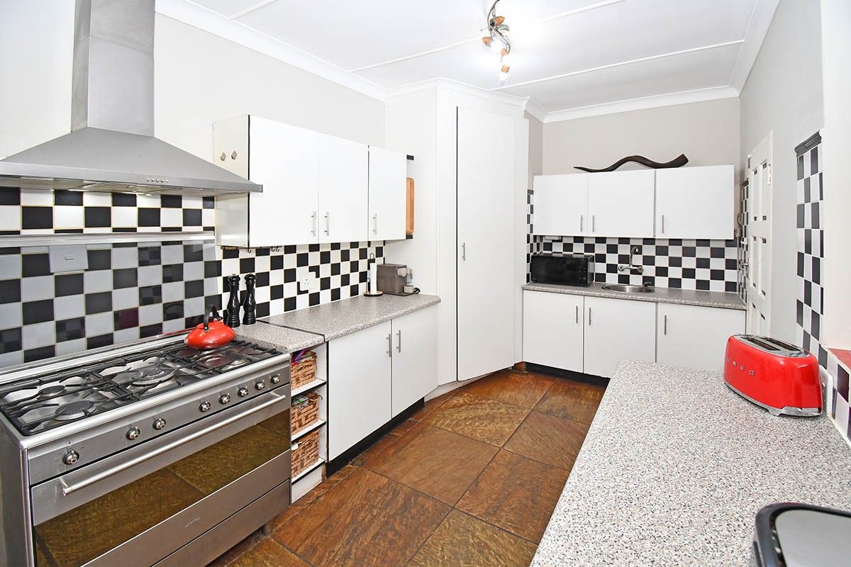 A functional kitchen featuring white cabinetry, granite countertops, a gas stove with extractor fan, and a distinctive black and white checkered tile backsplash.