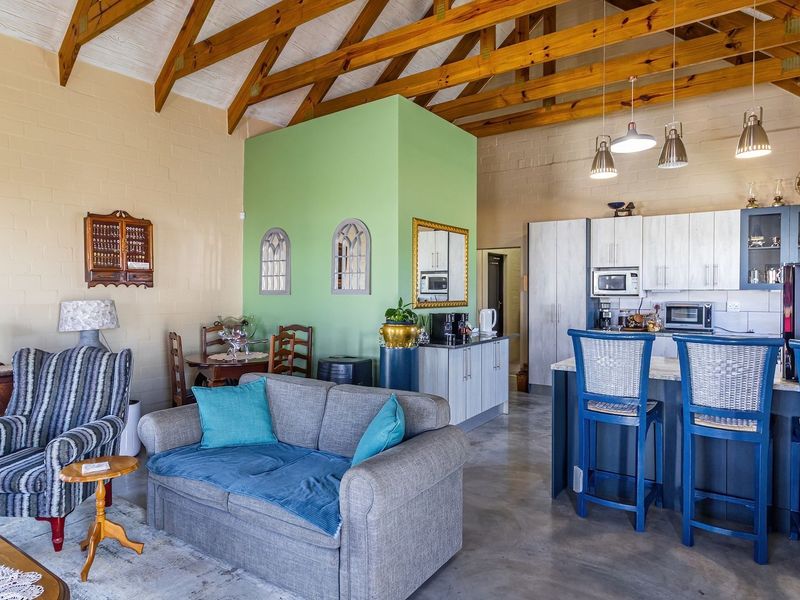 Spacious open-plan living and kitchen area featuring high vaulted ceilings with exposed timber rafters and polished concrete flooring.