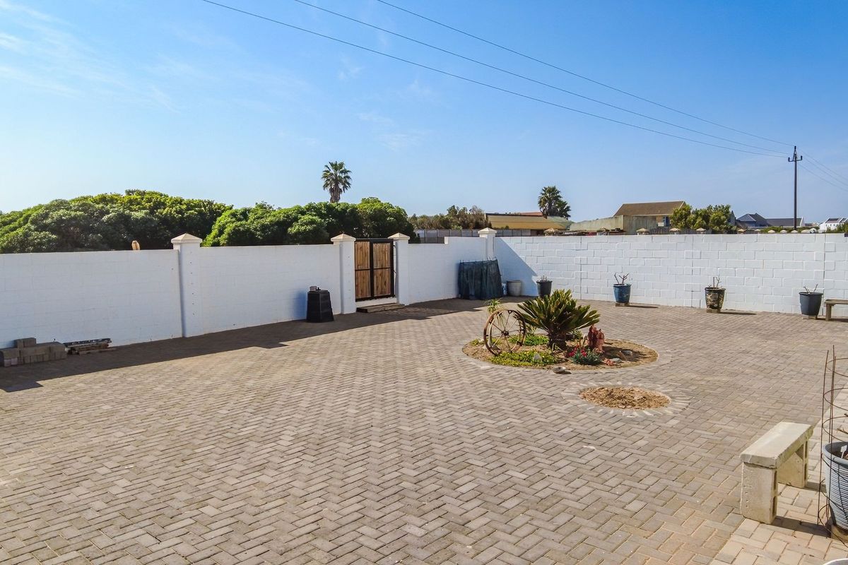 A spacious, paved rear courtyard enclosed by a white perimeter wall, featuring a central landscaped garden bed and a pedestrian access gate.