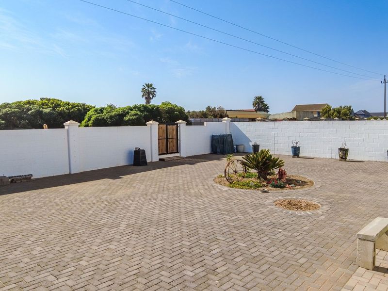 A spacious, paved rear courtyard enclosed by a white perimeter wall, featuring a central landscaped garden bed and a pedestrian access gate.