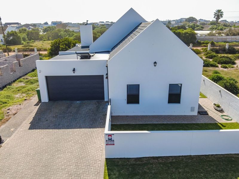 Aerial view of a modern single-story house featuring a paved driveway, double garage, and perimeter boundary wall in a residential setting.