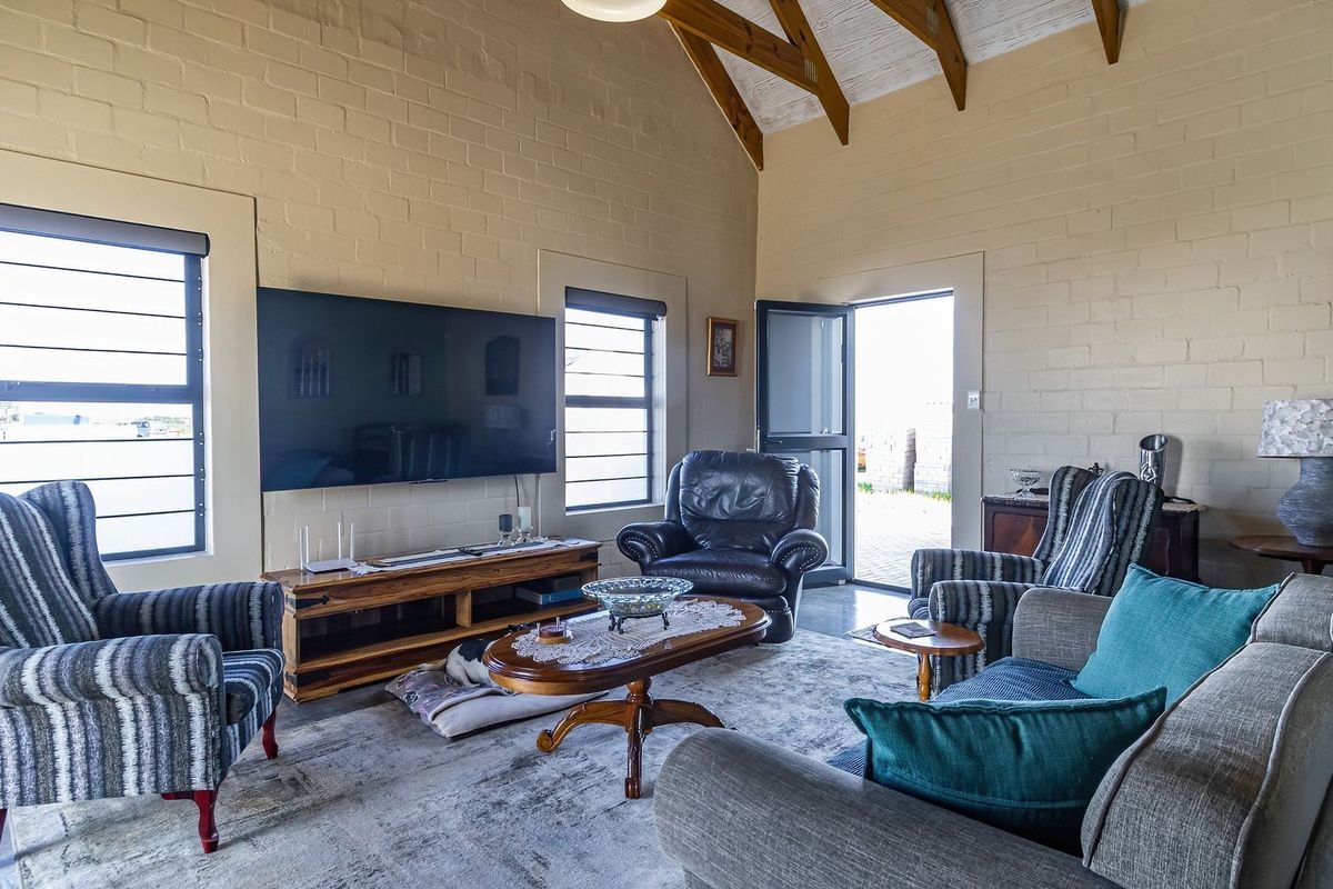 Spacious living room featuring high vaulted ceilings with exposed timber rafters, painted brick walls, and large windows providing natural light.
