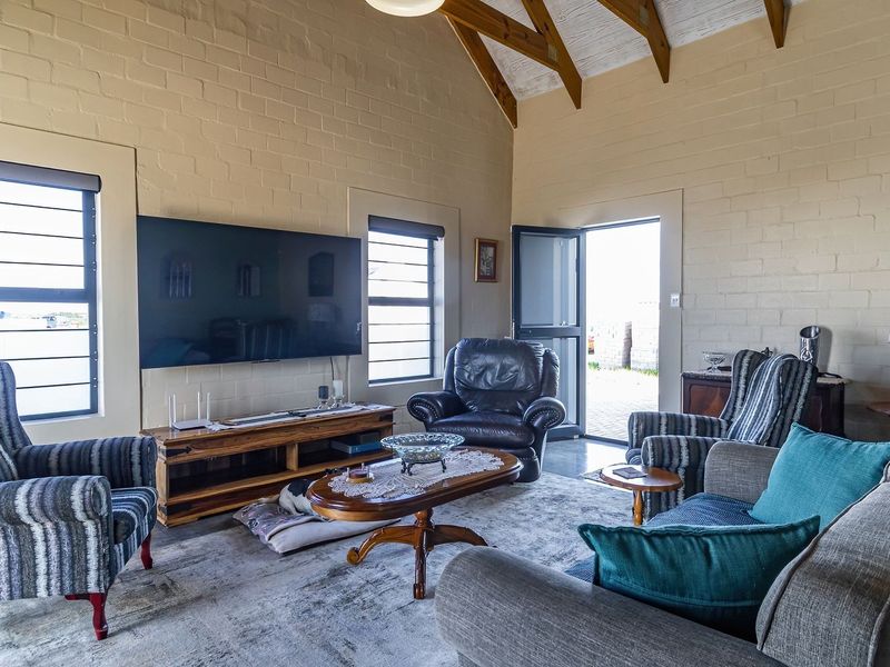 Spacious living room featuring high vaulted ceilings with exposed timber rafters, painted brick walls, and large windows providing natural light.