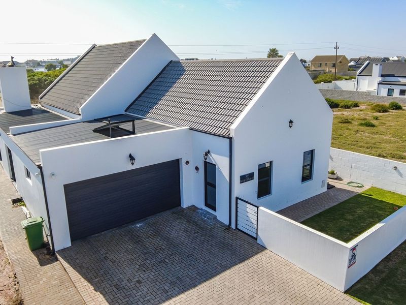 Aerial view of a modern white house featuring a tiled roof, double garage, paved driveway, and a private enclosed garden area.