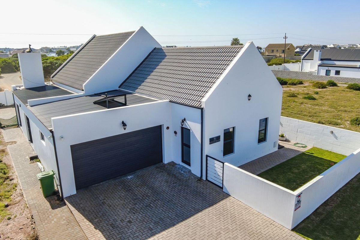 Aerial view of a modern white house featuring a tiled roof, double garage, paved driveway, and a private enclosed garden area.