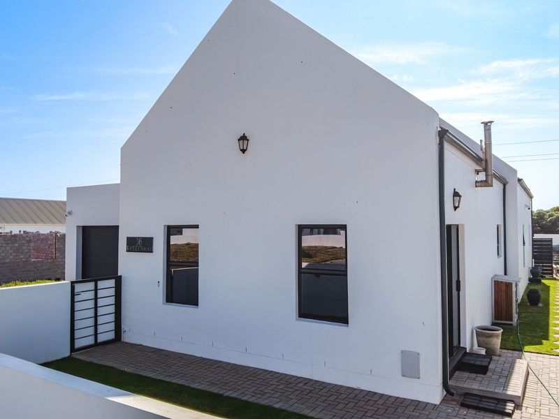 A modern white-painted house with a pitched roof, featuring a paved entrance area, boundary walls, and external lighting.