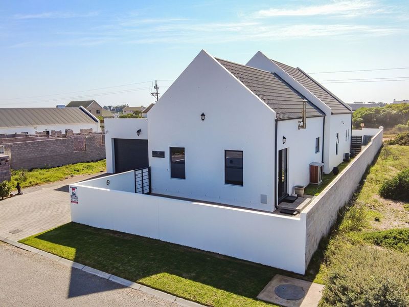 Aerial view of a modern white house with a tiled roof, featuring a paved driveway, garage, and perimeter boundary wall.